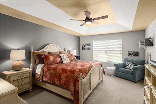 carpeted bedroom with a tray ceiling, a textured ceiling, and ceiling fan