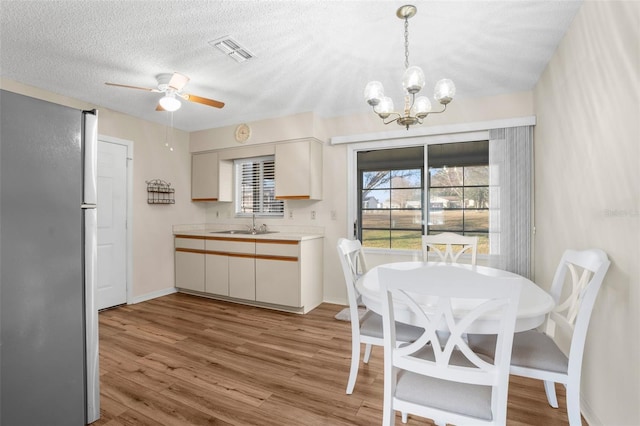 dining space featuring a textured ceiling, ceiling fan with notable chandelier, light wood-type flooring, and sink