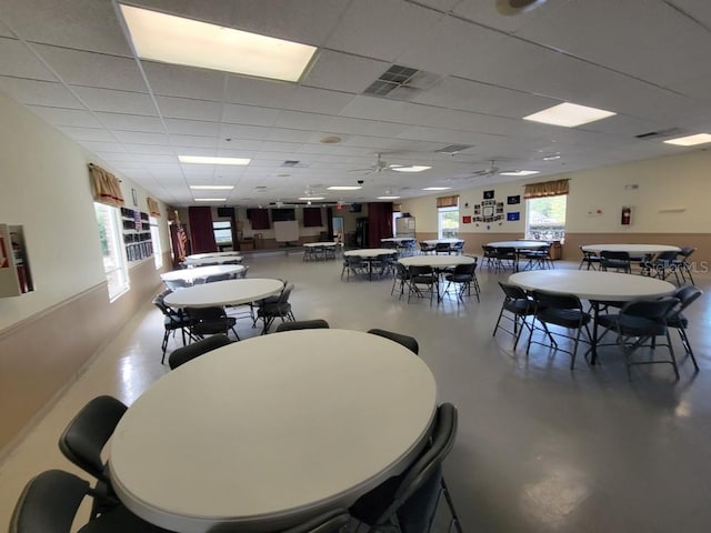 dining area featuring ceiling fan, a drop ceiling, and concrete floors