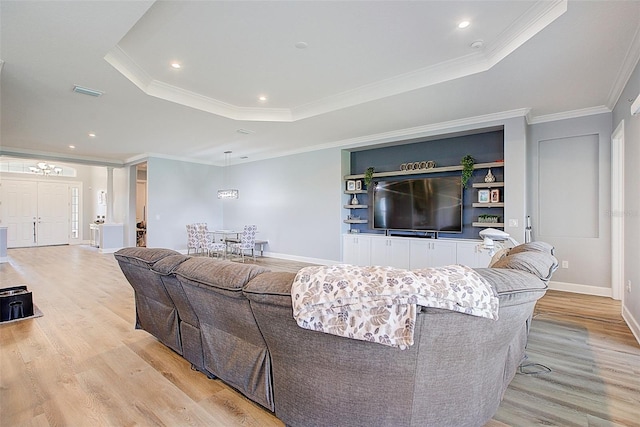 living room with a raised ceiling, crown molding, and light hardwood / wood-style flooring