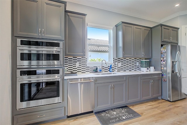 kitchen featuring sink, tasteful backsplash, gray cabinets, appliances with stainless steel finishes, and light wood-type flooring