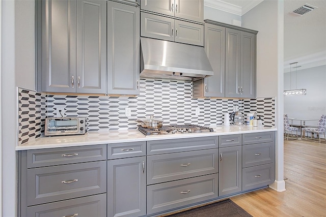 kitchen with tasteful backsplash, ornamental molding, light hardwood / wood-style floors, stainless steel gas cooktop, and gray cabinets