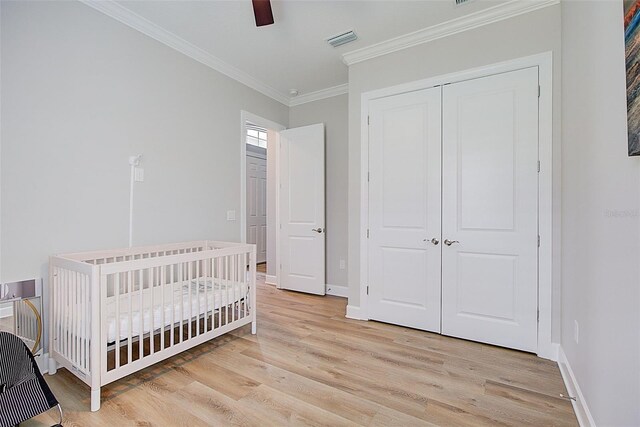 bedroom featuring ceiling fan, light hardwood / wood-style flooring, a closet, a nursery area, and ornamental molding