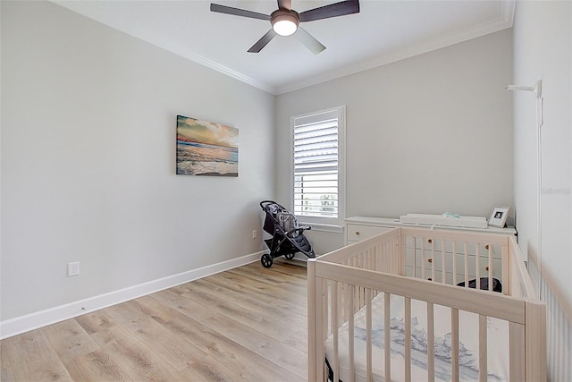 bedroom featuring light wood-type flooring, a nursery area, crown molding, and ceiling fan