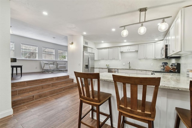 kitchen with kitchen peninsula, appliances with stainless steel finishes, light stone countertops, sink, and white cabinetry