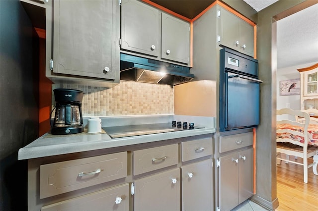 kitchen featuring black appliances, gray cabinets, light wood-type flooring, and backsplash