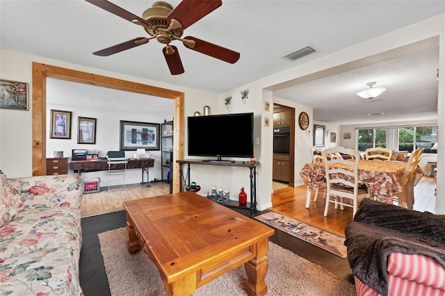 living room with a textured ceiling, light hardwood / wood-style flooring, and ceiling fan