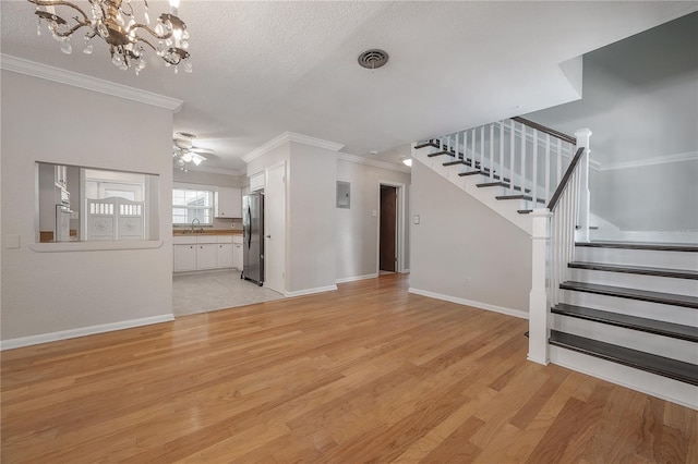 unfurnished living room featuring sink, crown molding, a textured ceiling, light wood-type flooring, and ceiling fan with notable chandelier