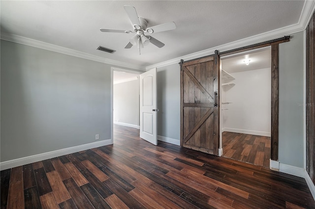 unfurnished bedroom with dark wood-type flooring, ceiling fan, ornamental molding, and a barn door