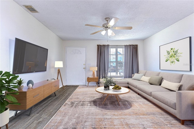 living room featuring dark hardwood / wood-style floors, ceiling fan, and a textured ceiling