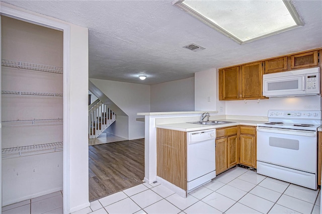 kitchen with sink, kitchen peninsula, a textured ceiling, white appliances, and light tile patterned floors