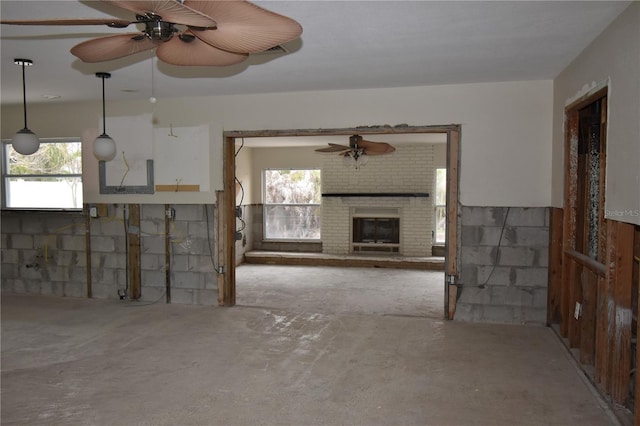 unfurnished living room featuring a fireplace, ceiling fan, and a healthy amount of sunlight