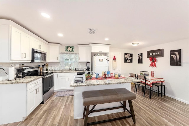 kitchen with appliances with stainless steel finishes, light wood-type flooring, light stone counters, white cabinets, and a center island