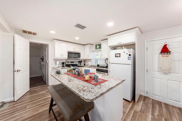 kitchen with white cabinetry, light stone counters, a kitchen bar, a kitchen island, and appliances with stainless steel finishes