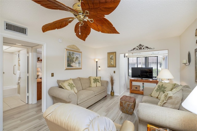 living room featuring ceiling fan, a textured ceiling, and light wood-type flooring