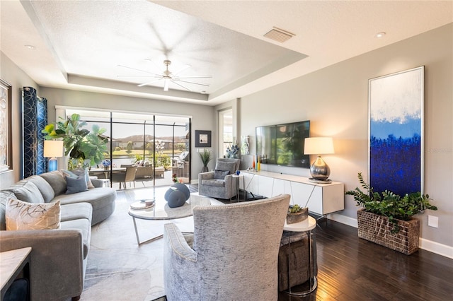 living room with ceiling fan, dark hardwood / wood-style floors, a textured ceiling, and a tray ceiling