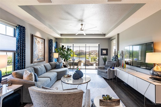 living room featuring a textured ceiling, a raised ceiling, plenty of natural light, and ceiling fan