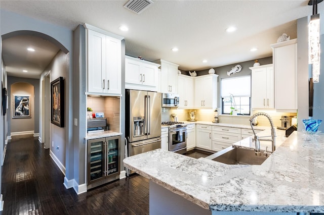 kitchen with tasteful backsplash, high end appliances, beverage cooler, sink, and white cabinetry