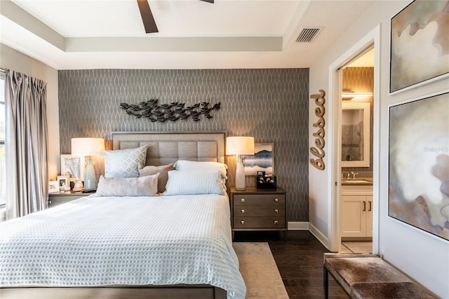 bedroom with connected bathroom, a raised ceiling, ceiling fan, and dark wood-type flooring