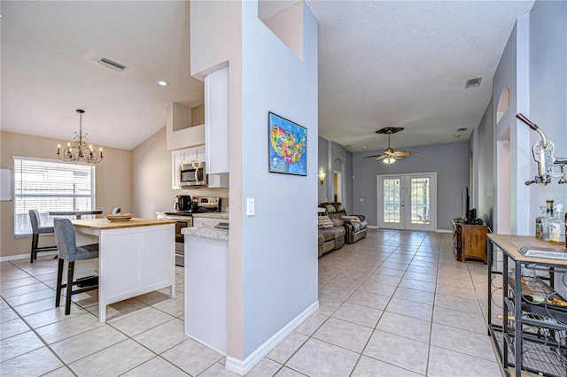 kitchen featuring white cabinets, appliances with stainless steel finishes, ceiling fan with notable chandelier, and light tile patterned floors