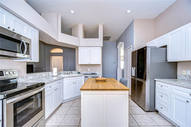 kitchen with kitchen peninsula, light stone counters, stainless steel appliances, a center island, and white cabinetry