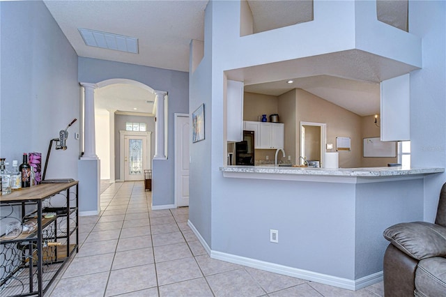 kitchen with white cabinets, kitchen peninsula, light tile patterned floors, and ornate columns