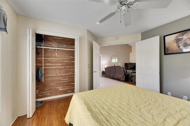 bedroom with a textured ceiling, wooden walls, a closet, light wood-type flooring, and ceiling fan