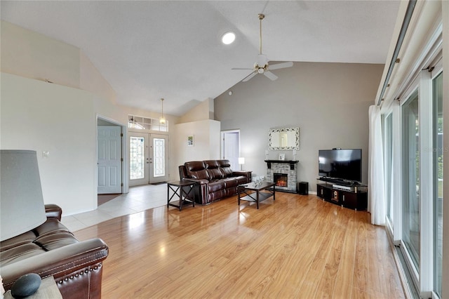 living room with ceiling fan, a fireplace, light wood-type flooring, high vaulted ceiling, and french doors