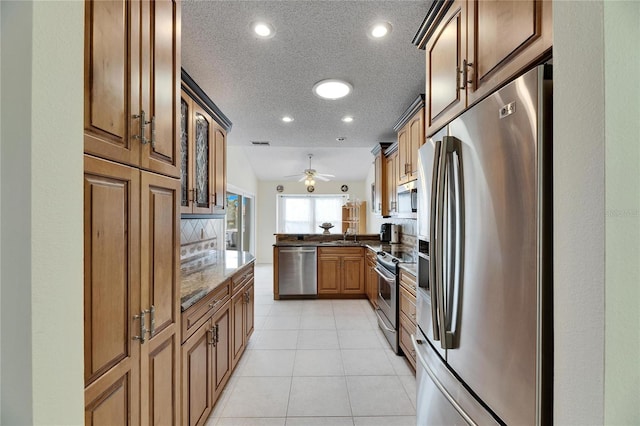 kitchen with ceiling fan, kitchen peninsula, appliances with stainless steel finishes, a textured ceiling, and dark stone counters