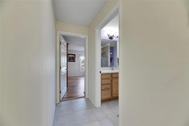 hall featuring a textured ceiling, light tile patterned floors, a chandelier, and sink