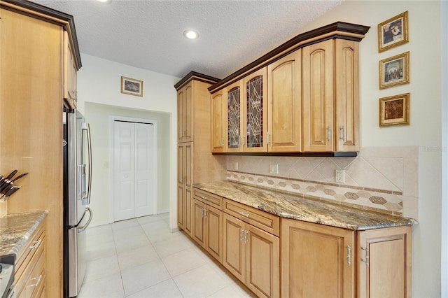 kitchen with a textured ceiling, decorative backsplash, stainless steel fridge, and light stone counters