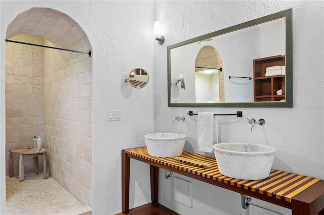 bathroom featuring a tile shower and double sink