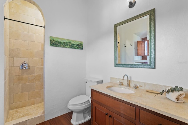 bathroom with a tile shower, vanity, toilet, and hardwood / wood-style floors