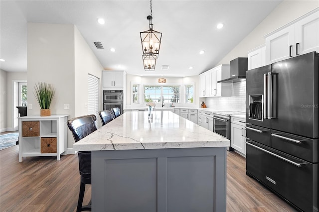 kitchen featuring a kitchen island, appliances with stainless steel finishes, a breakfast bar area, and wall chimney range hood