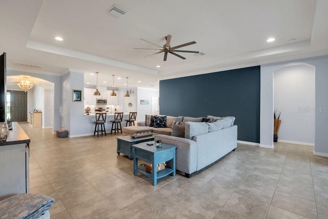 living area featuring arched walkways, visible vents, baseboards, and a tray ceiling