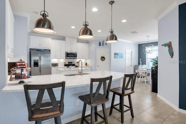 kitchen with pendant lighting, white cabinets, sink, appliances with stainless steel finishes, and a breakfast bar area