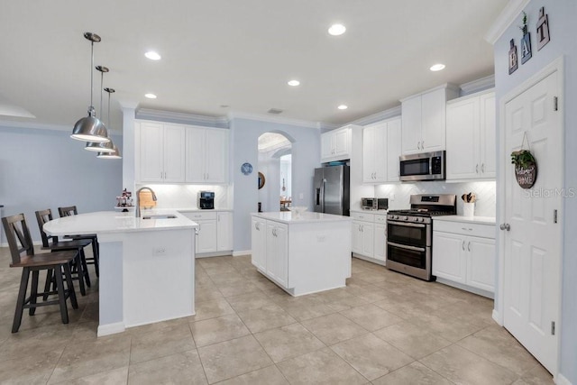 kitchen featuring an island with sink, arched walkways, appliances with stainless steel finishes, and ornamental molding