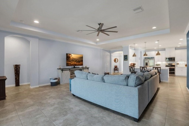 living area featuring visible vents, recessed lighting, arched walkways, a raised ceiling, and a ceiling fan