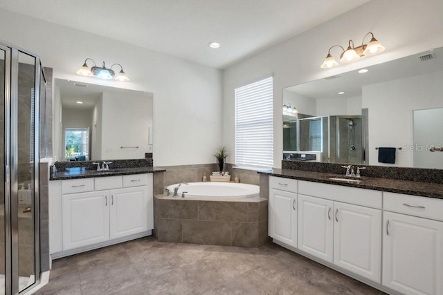 full bathroom featuring visible vents, two vanities, a sink, a shower stall, and a garden tub