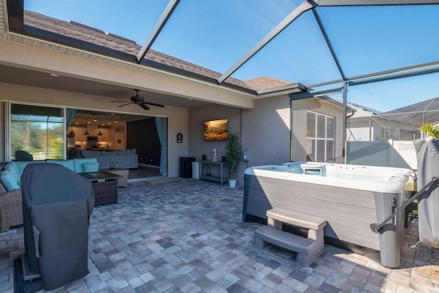 view of patio with glass enclosure, ceiling fan, and a hot tub