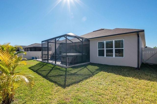 rear view of house featuring a shingled roof, glass enclosure, stucco siding, a yard, and a fenced backyard