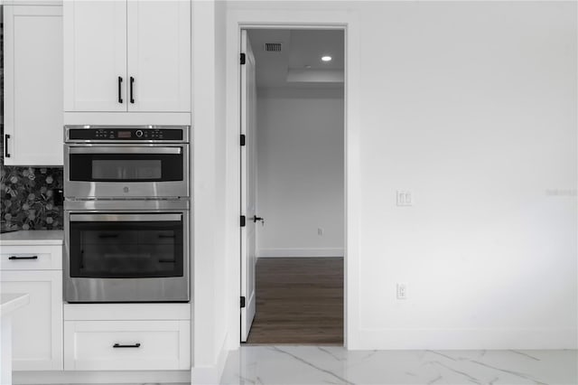 kitchen featuring baseboards, marble finish floor, double oven, white cabinetry, and backsplash