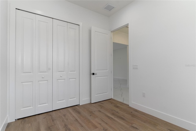 unfurnished bedroom with baseboards, visible vents, a closet, and wood finished floors