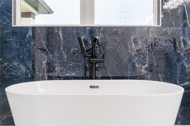 bathroom with marble finish floor, a freestanding bath, and a sink