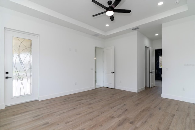 empty room with light hardwood / wood-style flooring, a raised ceiling, and ceiling fan