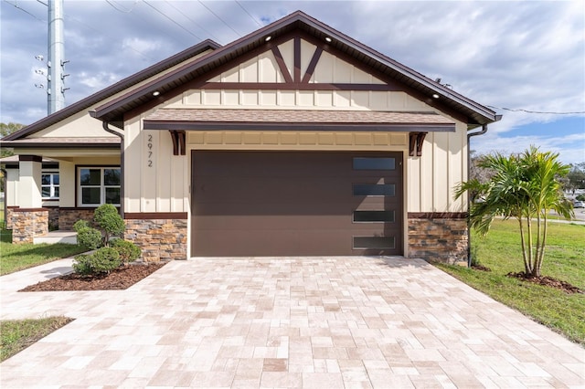 view of front facade featuring an attached garage, stone siding, decorative driveway, and board and batten siding