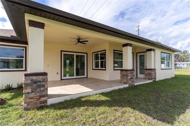 back of property with a patio, stucco siding, a lawn, a ceiling fan, and stone siding