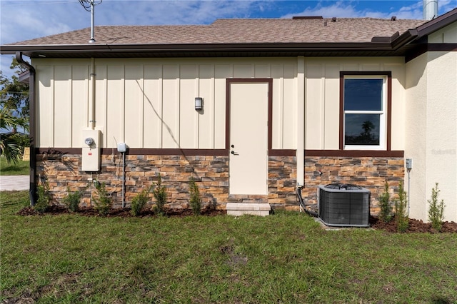 exterior space featuring cooling unit, stone siding, a lawn, roof with shingles, and board and batten siding