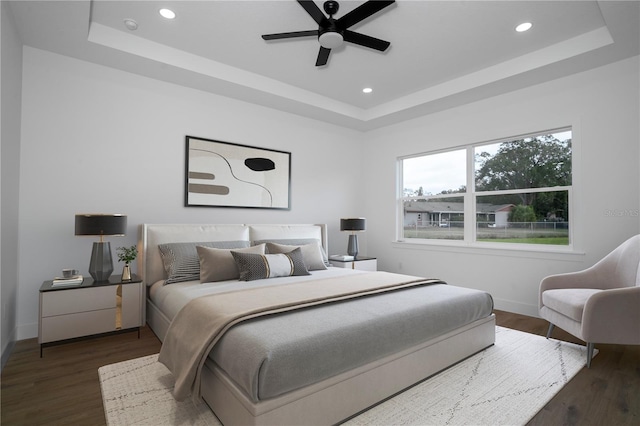 bedroom with a tray ceiling, baseboards, recessed lighting, and wood finished floors