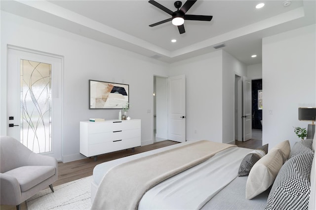 bedroom with baseboards, visible vents, wood finished floors, a tray ceiling, and recessed lighting